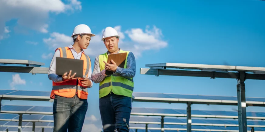 young-asian-technician-man-colleague-safety-uniform-checking-operation-sun-photovoltaic-solar-panel-use-laptop-computer-while-working-solar-farm